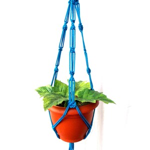 Puede incluir: Un macetero de macramé azul con una maceta de terracota y una planta verde.