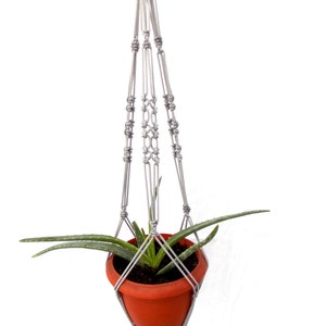 Puede incluir: Un macetero de macramé gris con una maceta pequeña de terracota y una planta suculenta verde en su interior.