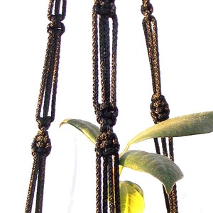May include: Black macrame plant hanger with three strands of rope. The hanger is knotted to create a sturdy and decorative design.