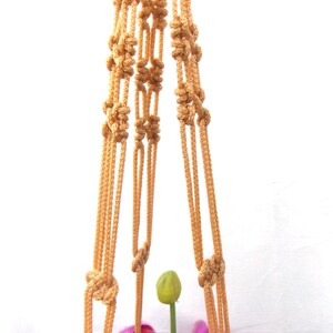 May include: A macrame plant hanger made of beige rope with a knotted design. The hanger is empty and ready to hold a potted plant.