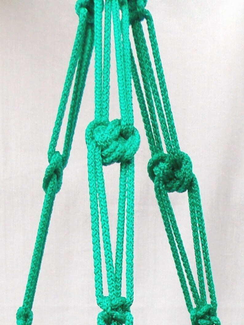 Pode incluir: Um close-up de um suporte de planta macram&ecirc; feito com corda turquesa. A corda &eacute; amarrada em um padr&atilde;o que cria uma forma triangular.