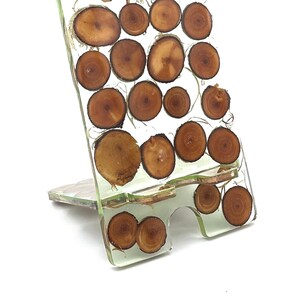 Pode incluir: Um suporte de telefone transparente feito de resina com fatias de madeira embutidas. O suporte é projetado para segurar um telefone na vertical.