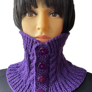 Könnte beinhalten: Lilafarbener gestrickter Halsschmuck mit Zopfmuster und vier großen lilafarbenen Knöpfen.