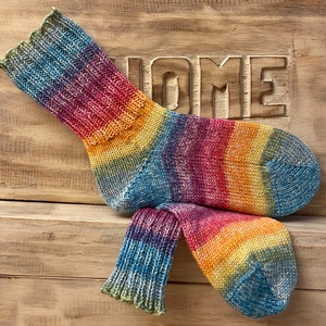 Könnte beinhalten: Ein Paar bunte gestreifte Socken in den Farben Blau, Gelb, Orange, Rot und Lila. Die Socken sind aus weichem, gestricktem Stoff und haben eine gerippte Struktur.