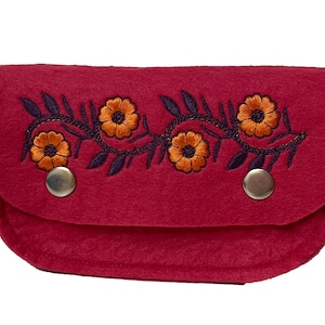 Könnte beinhalten: Eine kleine, rote Filz-Tasche mit einem floralen Muster, das in Orange und Lila gestickt ist. Die Tasche hat zwei silberne Druckknöpfe.