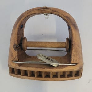 May include: A wooden yarn swift, a tool for winding yarn into a ball. The swift has a curved top, a horizontal wooden bar, and a series of vertical wooden pegs along the bottom. A metal piece is attached to the front.