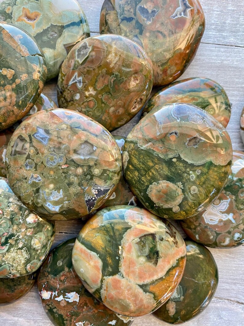 Puede incluir: Una colecci&oacute;n de piedras de jaspe oce&aacute;nico pulidas, cada una con patrones &uacute;nicos de verde, marr&oacute;n y naranja. Las piedras son lisas y tienen un acabado brillante.