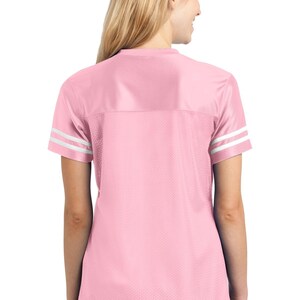 May include: A pink jersey with white stripes on the sleeves. The jersey is made of a mesh material and has a relaxed fit.
