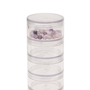 May include: A clear, stackable container with four compartments, each holding small, colourful beads. The beads are various shades of purple, pink, and clear. The container has a clear lid.