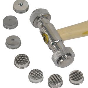 Op de afbeelding: Een zilveren metalen hamer met een houten handvat en verwisselbare koppen. De hamer heeft een verscheidenheid aan koppen, waaronder een ronde kop, een gewelfde kop en een getextureerde kop.