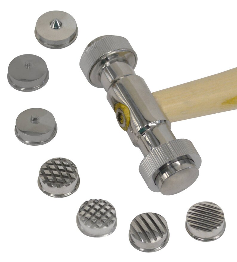 Op de afbeelding: Een zilveren metalen hamer met een houten handvat en verwisselbare koppen. De hamer heeft een verscheidenheid aan koppen, waaronder een ronde kop, een gewelfde kop en een getextureerde kop.