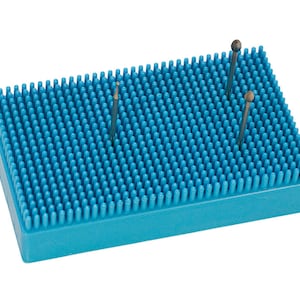 Könnte beinhalten: Ein blaues Nadelkissen mit einem Raster aus kleinen, blauen Gummiborsten. Drei Metallwerkzeuge sind in das Kissen gesteckt.