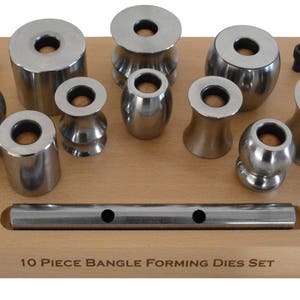Könnte beinhalten: Ein Satz von 10 Metall-Bangles-Formwerkzeugen auf einer Holzbasis. Die Werkzeuge sind in zwei Reihen angeordnet, mit einer Metallstange, die über die Basis verläuft. Der Text "10 PIECE BANGLES FORMING DIES SET" ist auf die Basis gedruckt.