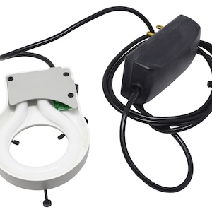 May include: A white, circular fluorescent light fixture with two curved bulbs, a silver mounting plate, and a black power cord. A black power adapter is also visible.