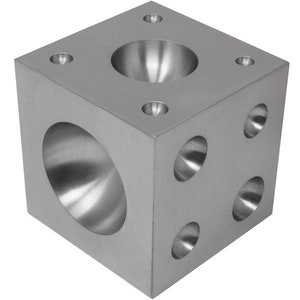 May include: A silver metal cube with five rounded depressions on each side. The cube is used for shaping metal.