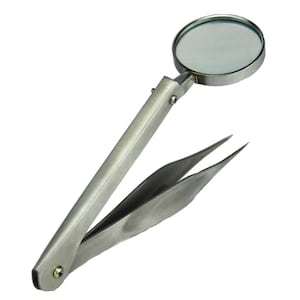 May include: A silver magnifying glass with tweezers attached to the handle. The magnifying glass is round and has a clear lens. The tweezers are closed and are made of metal.