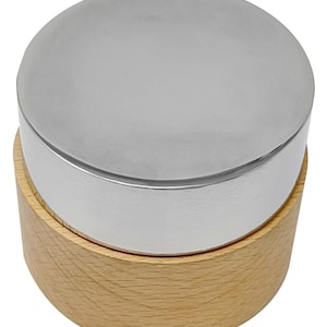 May include: A round wooden box with a silver lid. The lid is smooth and shiny. The box is made of light wood.