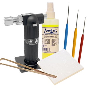 May include: A jewelry making kit with a black torch, a bottle of yellow Aquiflux hard soldering flux, four soldering picks, a pair of brass tweezers, and a white ceramic soldering block.