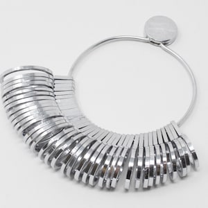 May include: A silver ring sizer with a circular base and a series of graduated rings. The rings are arranged in a fan shape and are numbered from 1 to 30.