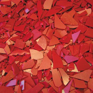 May include: A close-up image of a pile of red wax flakes. The flakes are various sizes and shapes, and they are all a deep red color.