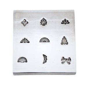 May include: A metal stamp with nine different designs, including a bow, a crescent moon, and various floral patterns.