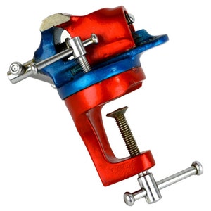 May include: A red and blue metal bench vise with a silver handle. The vise has a clamp on the bottom for attaching to a workbench.