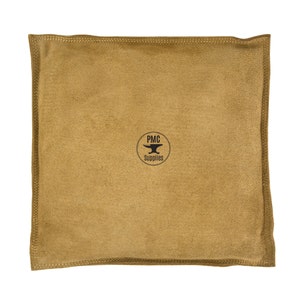 May include: A square, tan-colored suede leather bag with stitched edges. The bag features a circular logo in the center with the text "PMC Supplies" and an anvil graphic. The bag is likely used for storage or protection.