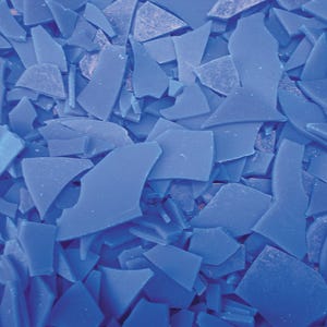 May include: A close-up of a pile of blue wax flakes. The flakes are irregular in shape and size, and they are all a vibrant blue colour.