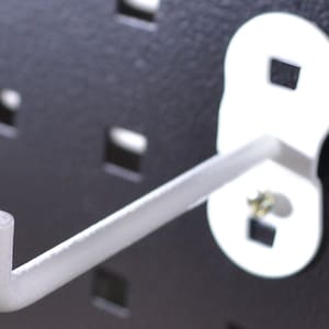 May include: White metal hook with a rounded base and a single hook. The hook is attached to a black pegboard.