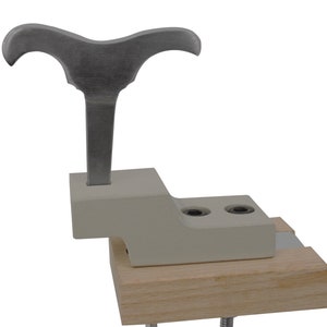 May include: A metal tool with a Y-shaped handle, mounted on a white base, which is attached to a wooden base. The tool is used for woodworking.