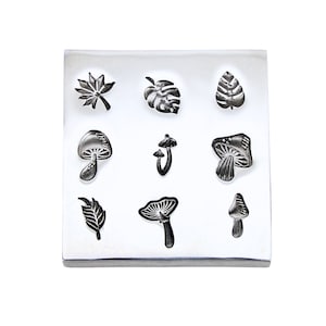 May include: A silver metal stamp with nine different designs, including mushrooms, leaves, and a monstera leaf. The designs are raised and ready to be used for crafting.