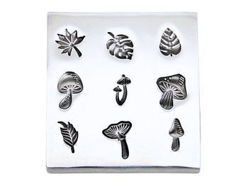 May include: A silver metal stamp with nine different designs, including mushrooms, leaves, and a monstera leaf. The designs are raised and ready to be used for crafting.