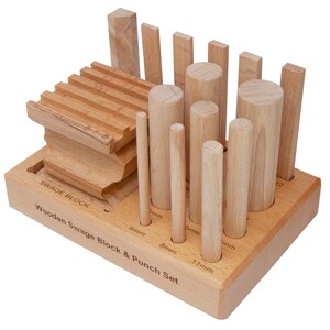 Puede incluir: Un juego de bloques de embutición y punzones de madera. El juego incluye una variedad de espigas de madera y bloques con forma, con el texto "SWAGE BLOCK" y "Wooden Swage Block & Punch Set" grabado en la base de madera. Las espigas están etiquetadas con tamaños en mm.