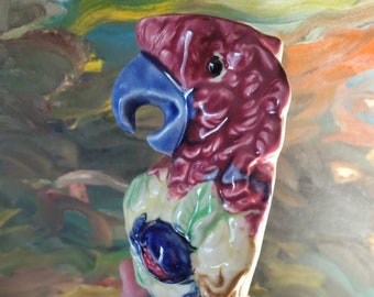 May include: A colorful ceramic parrot figurine with a blue beak, red, yellow, and green feathers, and a brown branch.