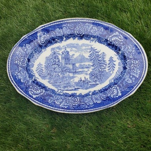 May include: A blue and white oval ceramic serving platter with a floral border and a central scene of a castle and mountains.