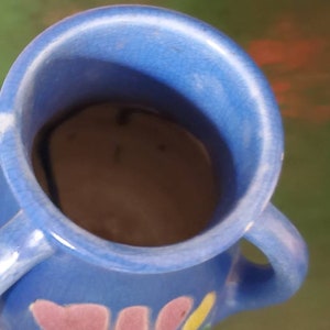 May include: A blue ceramic vase with two handles and a floral design. The vase has a pink, yellow, and green floral pattern.