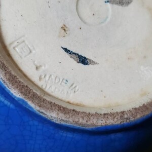 May include: Close-up of the bottom of a blue ceramic bowl with a white mark that reads "Made in Japan".