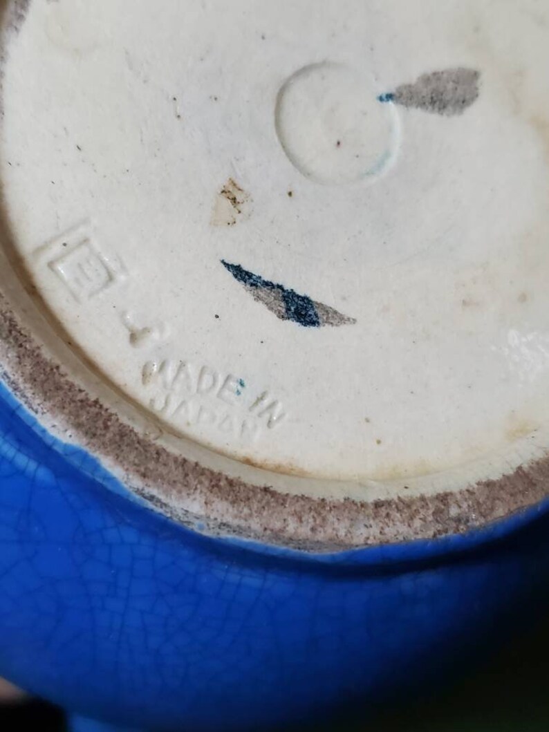 May include: Close-up of the bottom of a blue ceramic bowl with a white mark that reads "Made in Japan".
