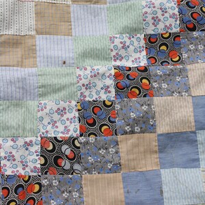 May include: A patchwork quilt made of various fabrics in shades of blue, green, brown, and white. The quilt is made up of squares of different patterns, including floral prints, geometric designs, and stripes.
