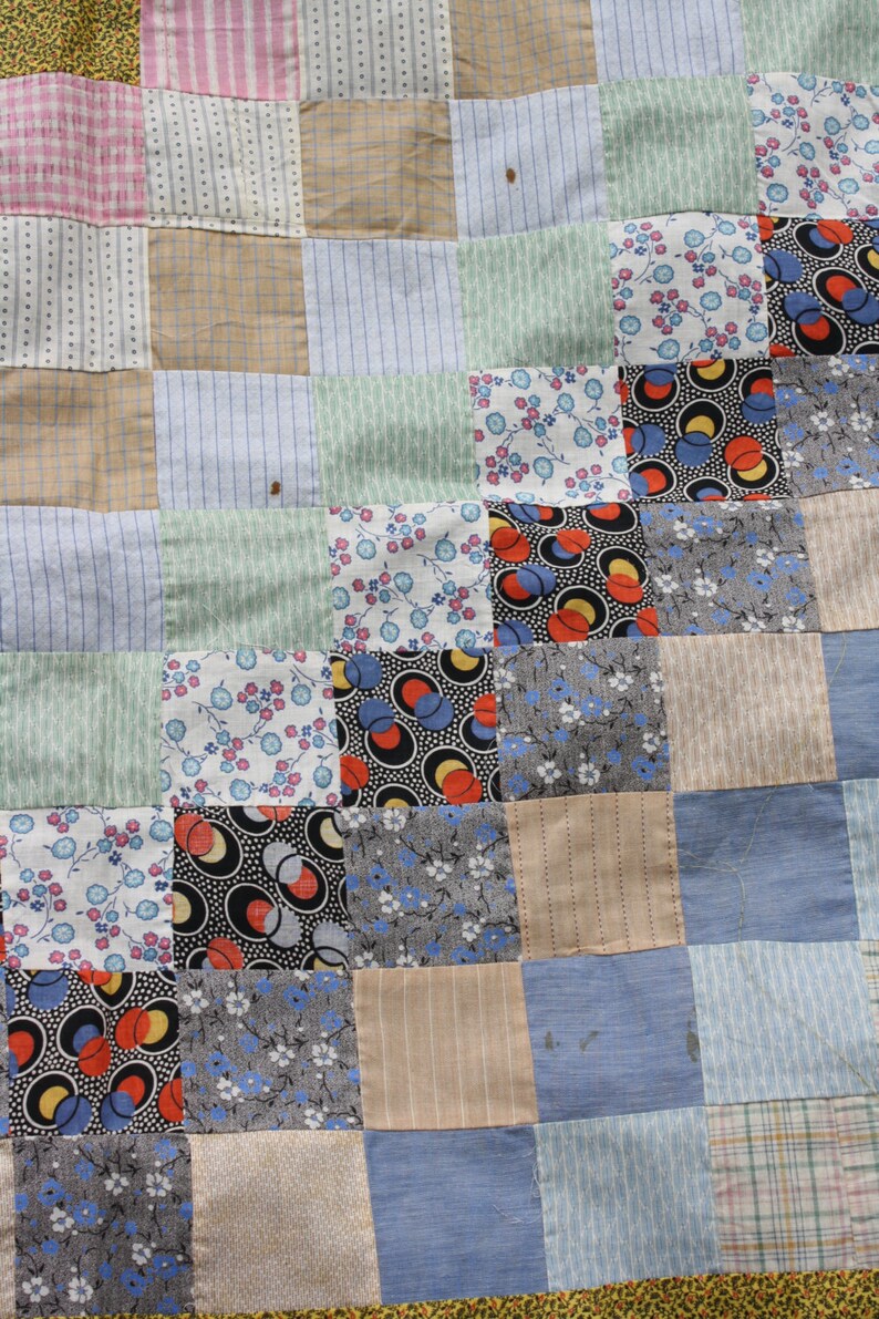 May include: A patchwork quilt made of various fabrics in shades of blue, green, brown, and white. The quilt is made up of squares of different patterns, including floral prints, geometric designs, and stripes.