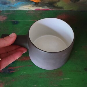 Op de afbeelding: Een donkergrijze keramische mok met een witte binnenkant. De mok heeft een afgeronde handgreep.