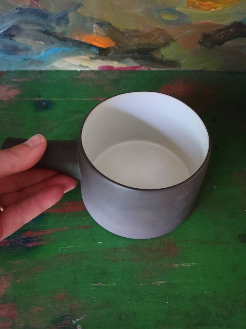 Op de afbeelding: Een donkergrijze keramische mok met een witte binnenkant. De mok heeft een afgeronde handgreep.
