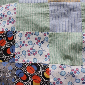 May include: A patchwork quilt with squares of different fabrics. The fabrics include a floral print, a geometric print, and a striped print. The quilt is made in a variety of colors, including blue, green, red, and white.