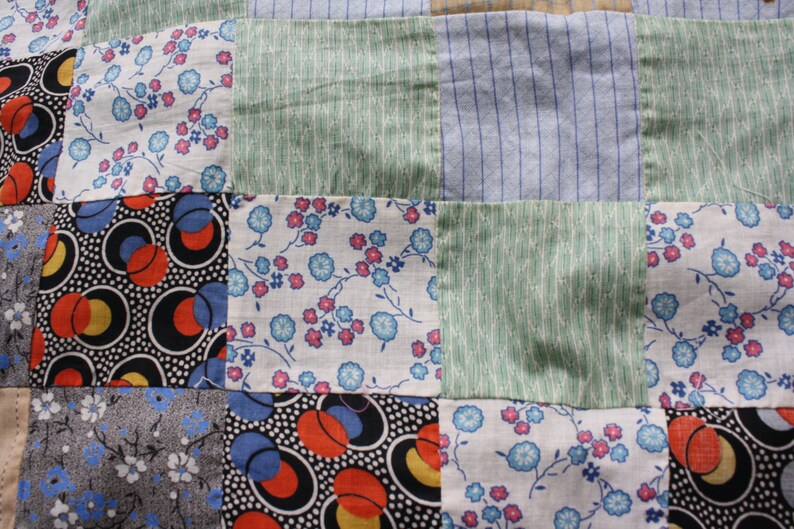 May include: A patchwork quilt with squares of different fabrics. The fabrics include a floral print, a geometric print, and a striped print. The quilt is made in a variety of colors, including blue, green, red, and white.