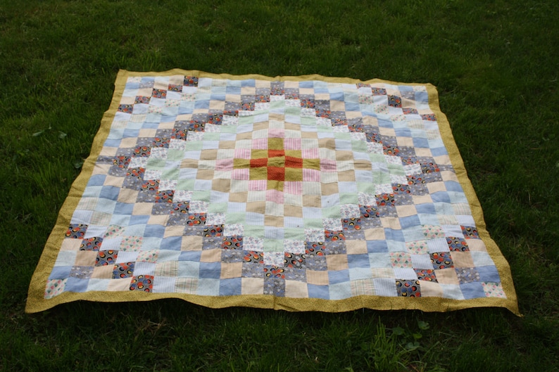 May include: A patchwork quilt with a diamond pattern in the center. The quilt is made of various fabrics in shades of blue, white, pink, and yellow. The center diamond is made of red, orange, and yellow fabrics.