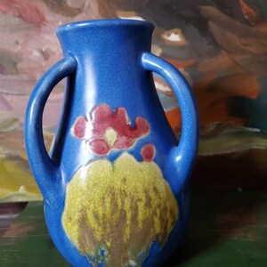 May include: A blue ceramic vase with two handles and a floral design. The vase has a crackled glaze and features a yellow and red flower design.