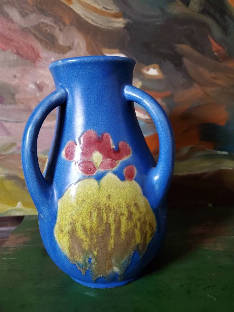 May include: A blue ceramic vase with two handles and a floral design. The vase has a crackled glaze and features a yellow and red flower design.