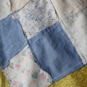 May include: A patchwork quilt with a variety of fabrics, including blue denim, white with a floral pattern, and a green and pink diamond pattern. The quilt is made up of squares sewn together.