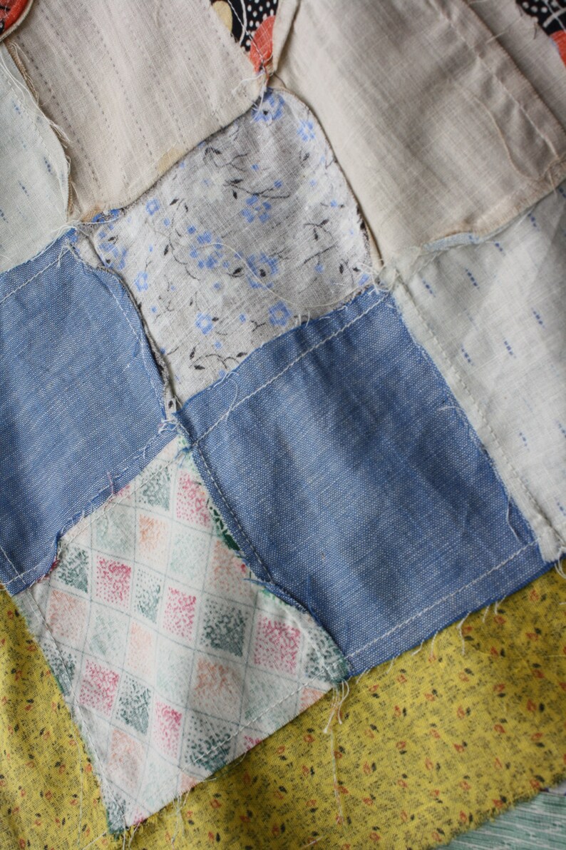 May include: A patchwork quilt with a variety of fabrics, including blue denim, white with a floral pattern, and a green and pink diamond pattern. The quilt is made up of squares sewn together.