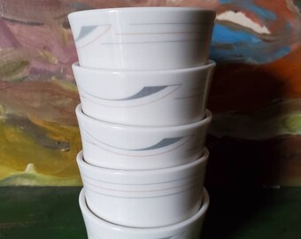 May include: A stack of five white ceramic bowls with a gray and brown geometric design. The bowls are stacked on a green surface.